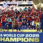 Rodri lifts the World Cup trophy, with Donald Trump and Gianni Infantino on stage to the right. Credit: Hannah McKay – Jul. 19, 2026/Reuters